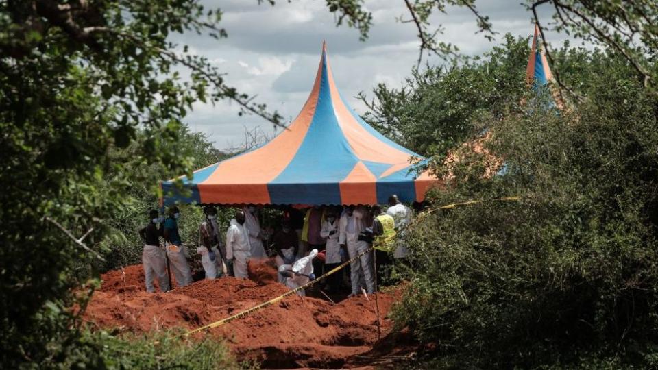 Workers take shelter as they dig the ground to exhume bodies from the mass grave in Shakahola