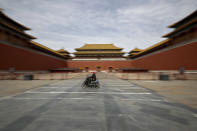 A man rides on an electric-powered scooter, passing by the closed entrance gates to the Forbidden City, usually crowded with tourists before the coronavirus outbreak in Beijing, Thursday, March 12, 2020. (AP Photo/Andy Wong)