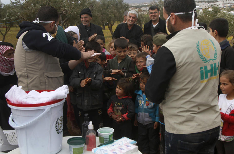 FILE - This file photo released by the Turkish humanitarian group IHH on April 6, 2020, aid workers of the group demonstrate to Syrian children how to properly wash hands, at a camp for internally displaced persons in northern Syria. The rapid spread of the coronavirus has raised fears about the world’s refugees and internally displaced people, many of whom live in poor or war-ravaged countries that are ill-equipped to test for the virus or contain a possible outbreak. (IHH via AP, File)