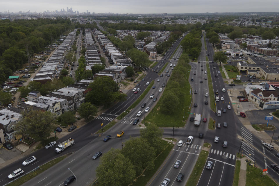 The Philadelphia skyline, top, is seen at a distance as vehicular traffic flows along Roosevelt Boulevard at the intersection with Whitaker Avenue, Thursday, May 12, 2022, in Philadelphia. Roosevelt Boulevard is an almost 14-mile maze of chaotic traffic patterns that passes through some of the city's most diverse neighborhoods and Census tracts with the highest poverty rates. Driving can be dangerous with cars traversing between inner and outer lanes, but biking or walking on the boulevard can be even worse with some pedestrian crossings longer than a football field and taking four light cycles to cross. (AP Photo/Julio Cortez)
