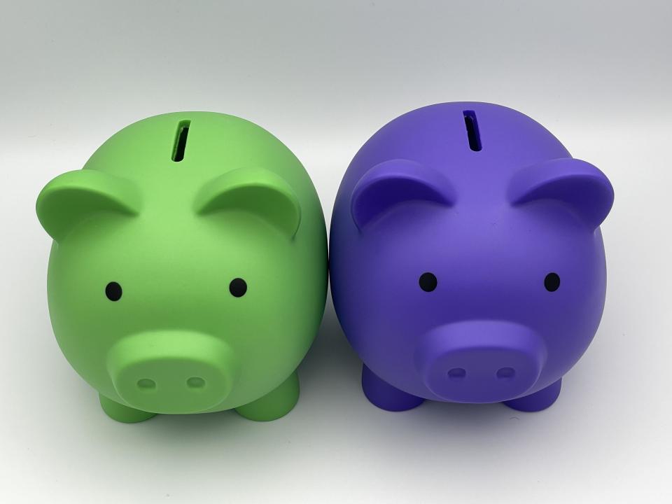 Two differently colored children’s piggy banks, purple and lime green, sitting side by side.