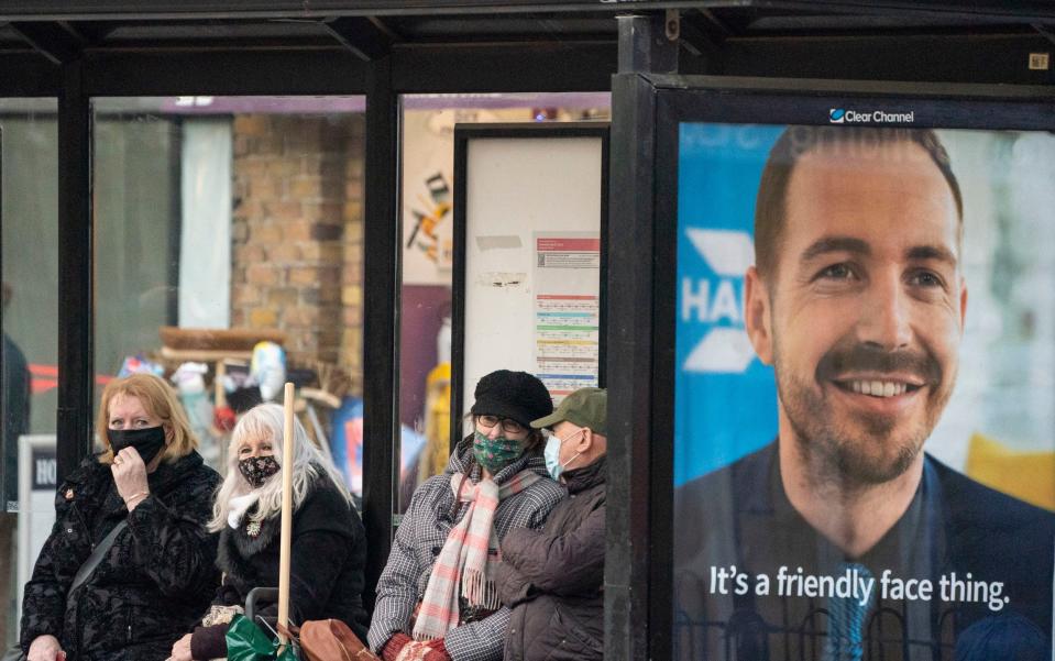 People wear face masks at a bus stop in Brentwood, Essex, on Monday as further cases of the omicron Covid variant were confirmed in the UK - Dominic Lipinski/PA Wire