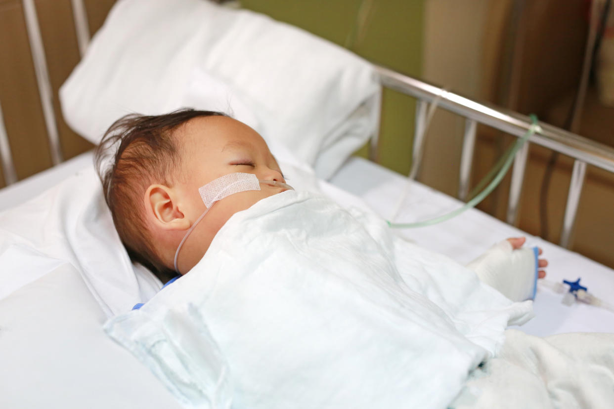 Baby boy with breathing tube in nose receiving medical treatment. Intensive care and attaching intravenous tube to hand on bed at hospital. Respiratory Syncytial Virus (RSV).