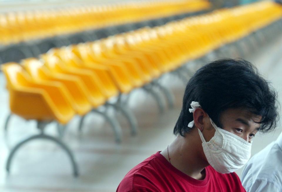 A Chinese traveller wearing a mask sits near sections of the waiting lounge that has been closed off due to a slump in passenger numbers at a train station in Beijing Thursday, May 22, 2003.