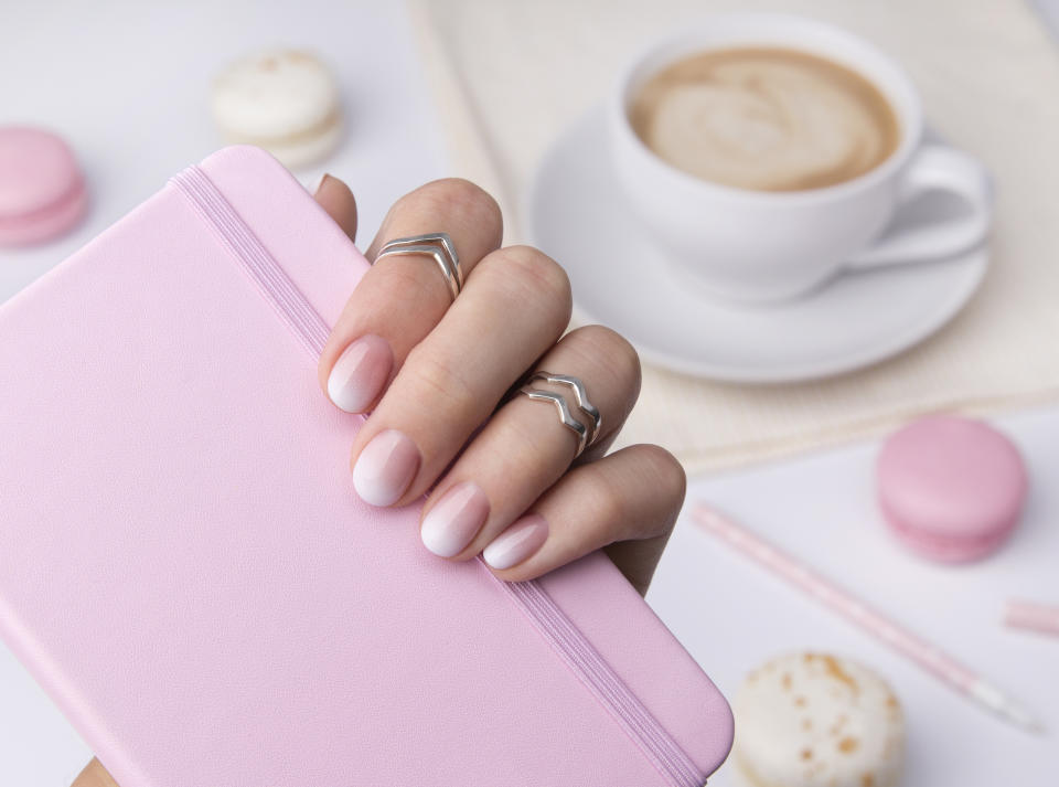 Beautiful manicured hand holding notepad at the office table. Ombre gradient nail design.