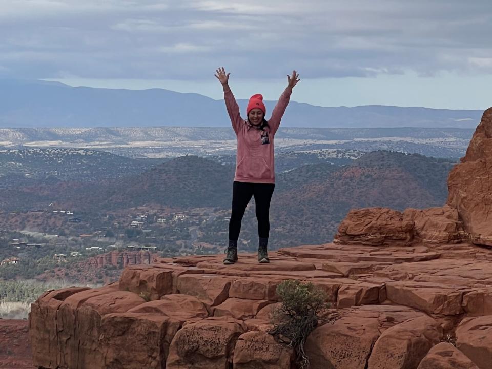 A woman standing on top of a scenic rock area with hands up in the sky.