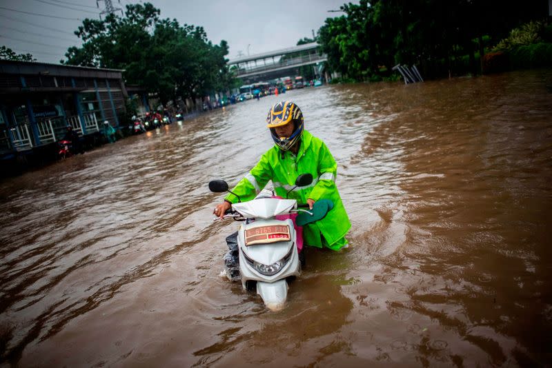 A man walks with his scooter through flood water after heavy rain in Jakarta