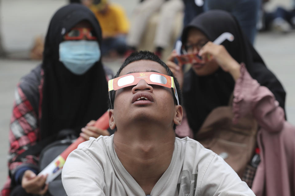People look up at the sun wearing protective glasses to watch a solar eclipse from Jakarta, Indonesia, Thursday, Dec. 26, 2019. (AP Photo/Tatan Syuflana)