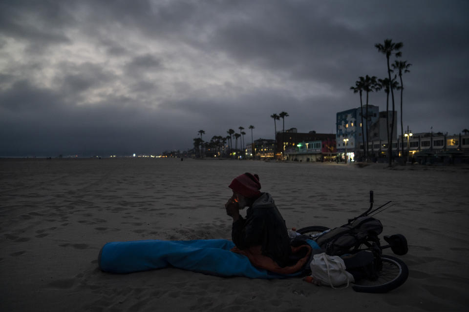 Kevin DeMarco, a 56-year-old homeless man, lights a cigarette in a sleeping bag on the beach Tuesday, June 29, 2021, in the Venice neighborhood of Los Angeles. The proliferation of homeless encampments on Venice Beach has sparked an outcry from residents and created a political spat among Los Angeles leaders. (AP Photo/Jae C. Hong)