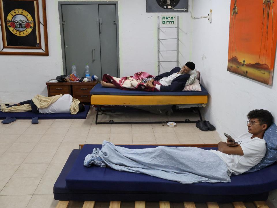 People take shelter during a rocket attack from the Gaza Strip. Two men lounge in beds in a sparsely-decorated concrete-reinforced room.