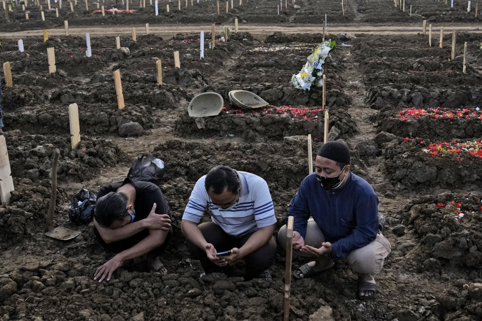 Men pray during the burial of a relative at Rorotan Cemetery which is reserved for those who died of COVID-19, in Jakarta, Indonesia, Thursday, July 1, 2021. New land around the capital city continues to be cleared for the dead and gravediggers have to work late shifts following surges in COVID-19 cases fueled by travel during the Eid holiday in May, and the spread of the delta variant of the coronavirus first found in India. (AP Photo/Dita Alangkara)