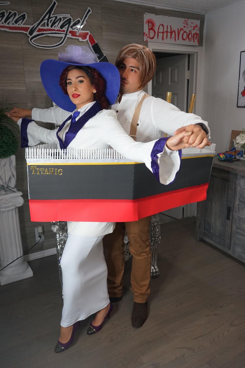 A couple dressed as Jack and Rose from "Titanic" pose inside of a cardboard boat.