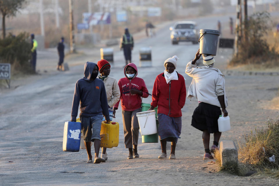 People carry buckets to fetch water past a police checkpoint in Harare, Friday, July, 31, 2020. Zimbabwe's capital, Harare, was deserted Friday, as security agents vigorously enforced the country's lockdown amidst planned protests. Police and soldiers manned checkpoints and ordered people seeking to get into the city for work and other chores to return home. (AP Photo/Tsvangirayi Mukwazhi)