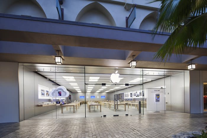 Apple Store location seen from outside in an open-air mall with a palm tree.