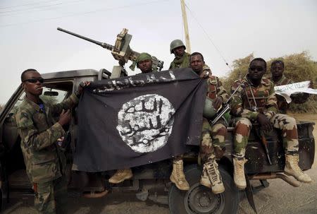 Nigerian soldiers hold up a Boko Haram flag that they had seized in the recently retaken town of Damasak, Nigeria, March 18, 2015. REUTERS/Emmanuel Braun