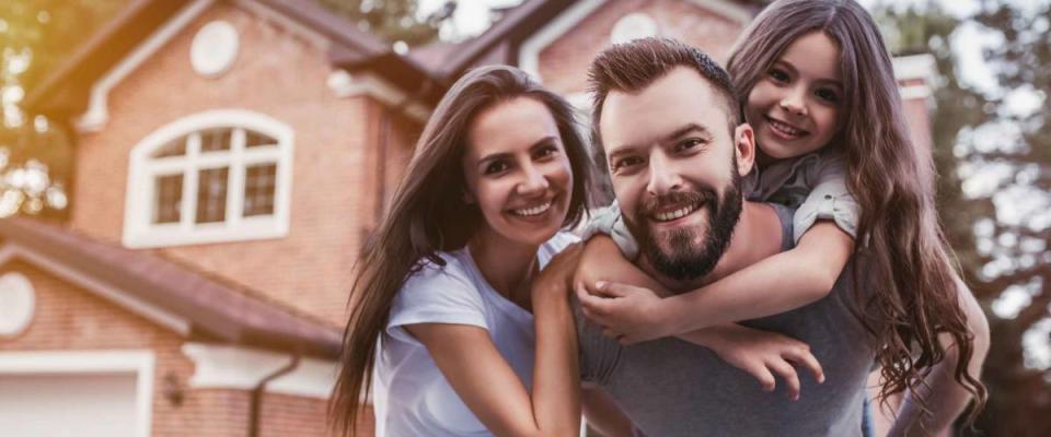 Happy family is standing near their modern house, smiling and looking at camera.