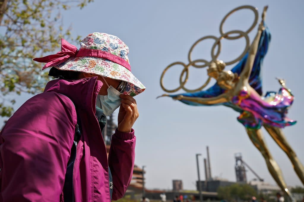 File: A woman adjusts her face mask as she walks by a statue featuring the Beijing Winter Olympics figure (AP)