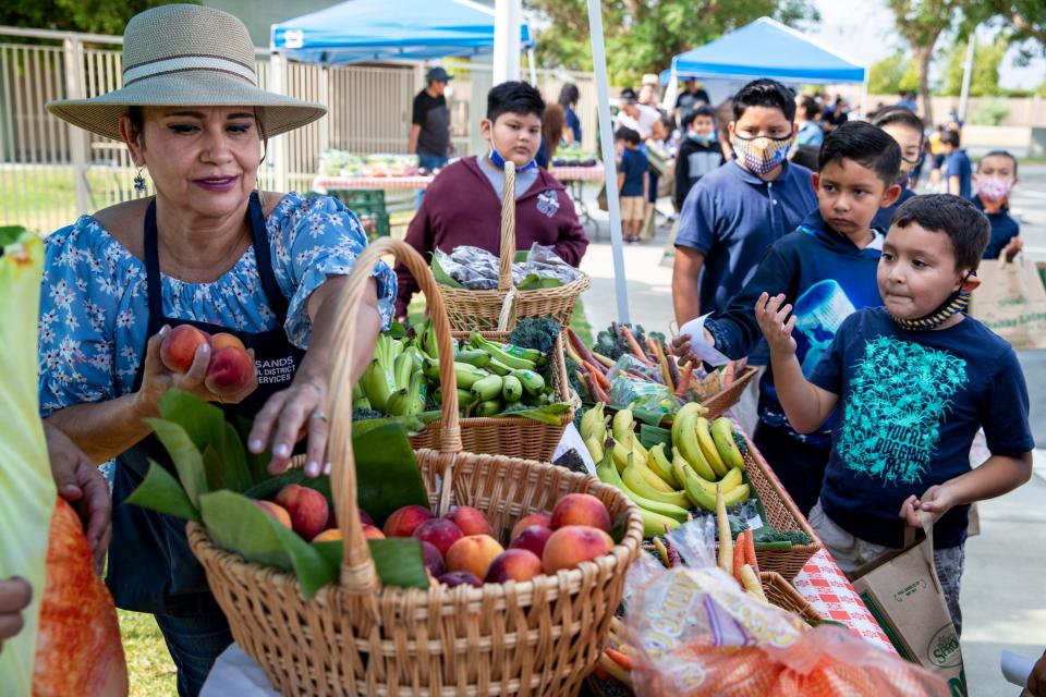 Bertha Celedon, left, sells peaches to students enrolled in Theodore Roosevelt Elementary School's summer program shop during a pop-up farmers market at the school in Indio, Calif., on June 29, 2021. The school provided each student with school market cash so they could purchase what they liked. 