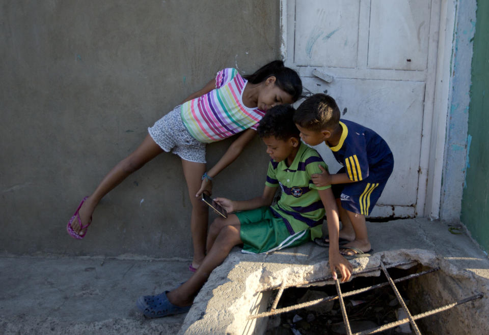 In this Dec. 10, 2018 photo, Solgreidy, 8, from left, Greider, 10, and Elvis, 3, speak with their mother Emili Espinoza, via an international video call outside their uncle's home in Punto Fijo, Venezuela. Espinoza left them with her brother in Venezuela in the hopes of earning enough money in Colombia, to feed them and, within time, reunite. (AP Photo/Fernando Llano)