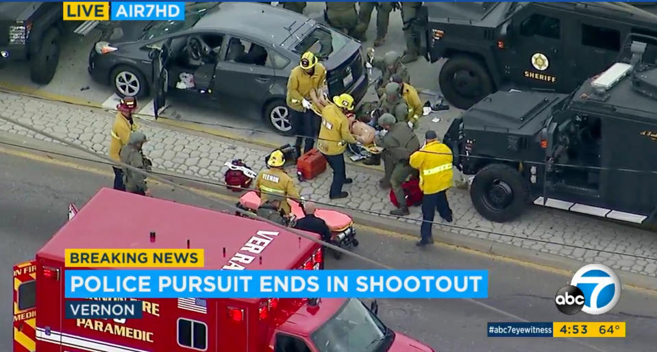 In this photo taken from video provided by KABC-TV, medics and officers tend to a wounded man after he was removed from his shot-up car, top left, at the conclusion of a wild car chase and rolling shootout in the Los Angeles area Friday afternoon, May 10, 2019. The car finally came to a halt in the Los Angeles suburb of Vernon, where the bloodied woman driver then got out and surrendered. The gunman remained in the car. The man, who appeared to be wounded, was removed from the car and taken to a hospital. His condition was not immediately known. (KABC-TV via AP)