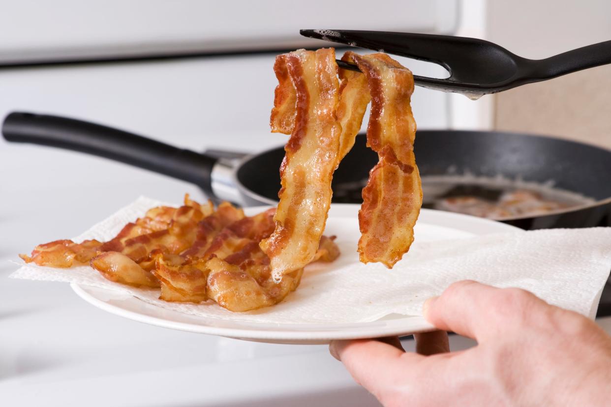 A close up of a spatula lifting a slice of bacon onto a plate