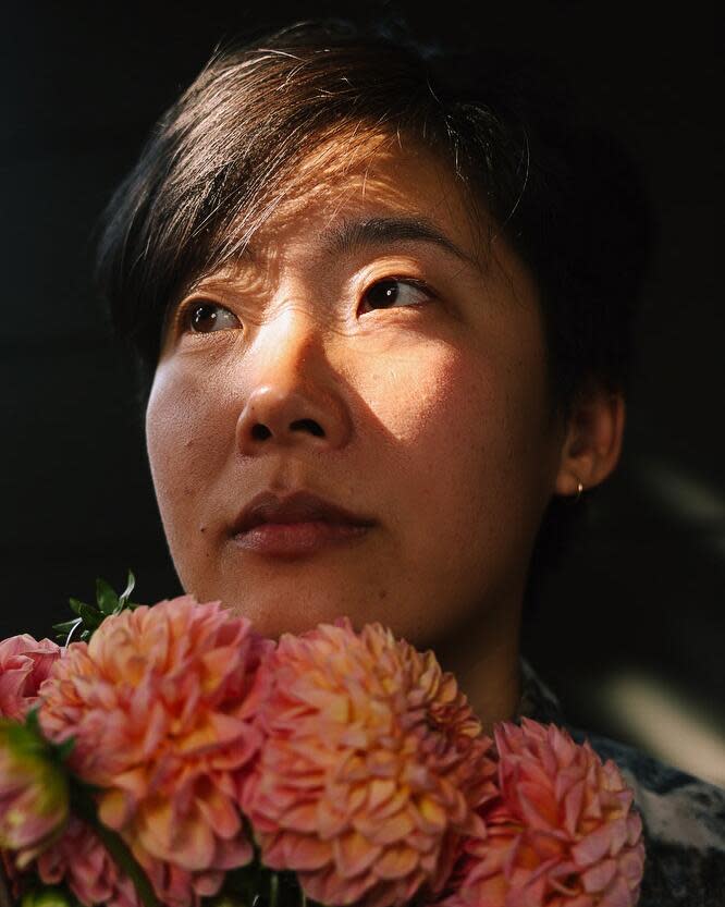 A person holding dahlias under their chin in their studio.