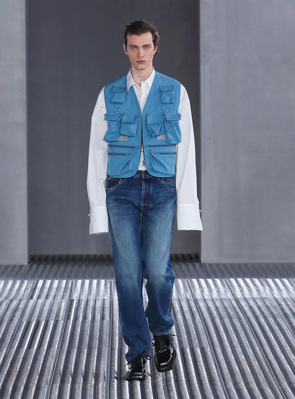 If Prada’s trend-setting history is any indication, the reporter vest—realized here in panama cotton—is about to be everywhere. Miuccia Prada and Raf Simons love to mess with ideas of formality. Paired with the vest and jeans, this white poplin maxi-cuff tuxedo shirt is completely recontextualized. These Japanese denim jeans, worn-in with a regular straight cut, speak to the designers’ sense of restraint. Mrs. Prada, who has long found style in ugliness, has practically single-handedly brought the square-toe dress shoe back into fashion. These derbies in black brushed leather are quintessential Prada.