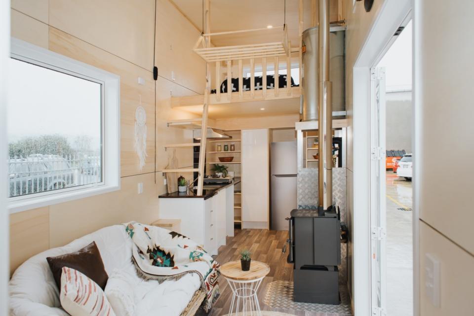 Lo primero que se encuentra en la vivienda es el salón, que está equipado con un sofá, una pequeña mesa de café y una estufa de leña. (Foto: <a href="http://www.buildtiny.co.nz/kahurangi-koinga-tiny-house" rel="nofollow noopener" target="_blank" data-ylk="slk:Build Tiny;elm:context_link;itc:0;sec:content-canvas" class="link ">Build Tiny</a>).