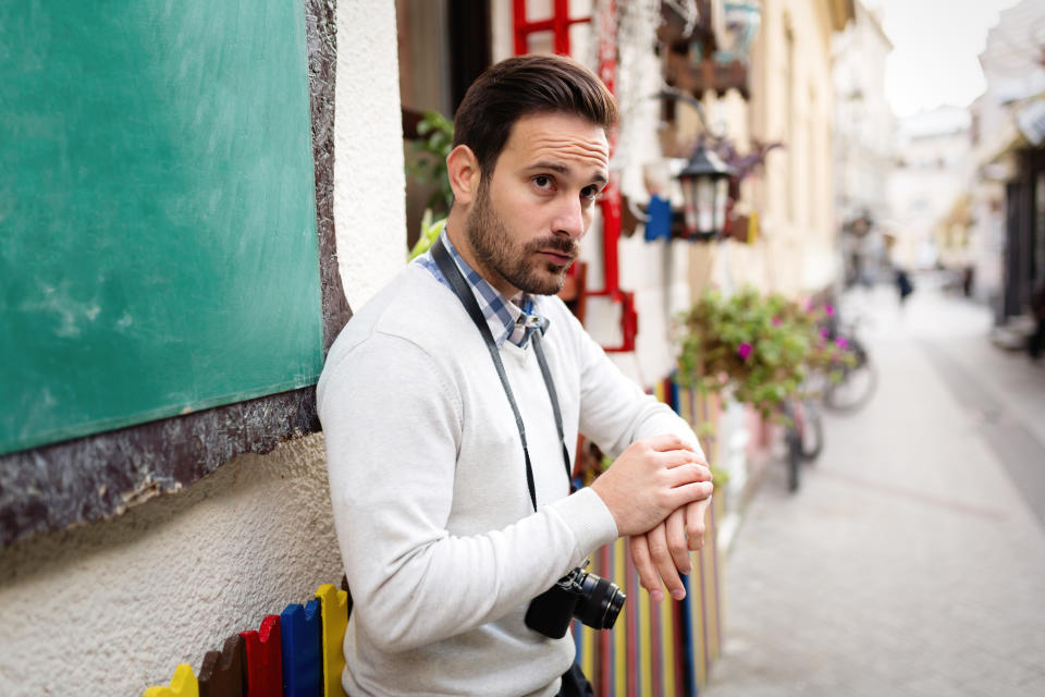 I don't know who the person is. The image shows a man leaning against a wall, holding a camera, looking thoughtful on a street