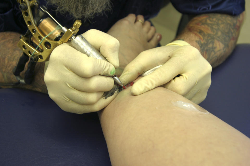 tattoo artist working on woman's ankle