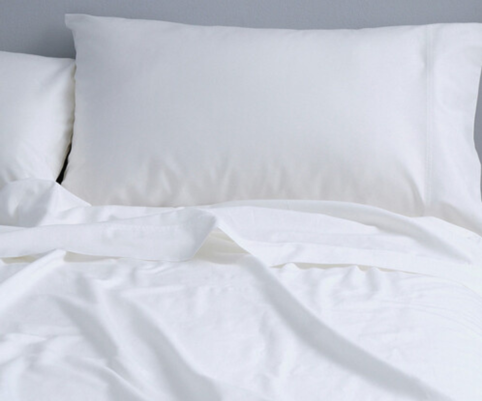 A white pillow sits upright on a bed with white crumpled sheets. 