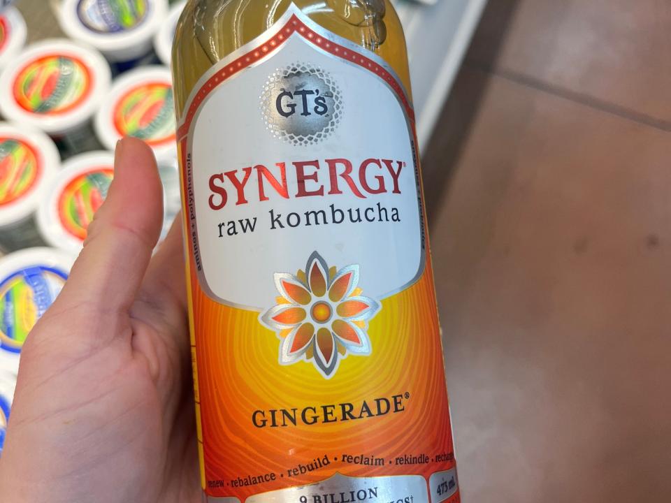 A hand holding a bottle of Synergy raw kombucha gingerade.