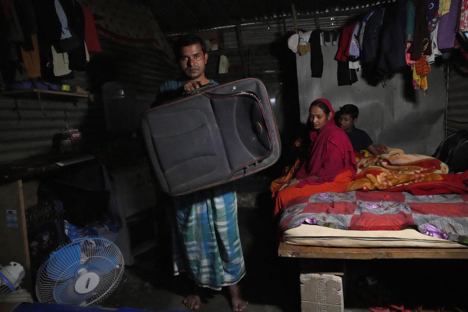 Climate refugee Jaidul Islam, left, holds up a large suitcase in which he carried some clothes for the kids, a mosquito net and two towels, when he left his flooded village with his family and migrated to this one room home in Bengaluru, India, Wednesday, July 20, 2022. (AP Photo/Aijaz Rahi)