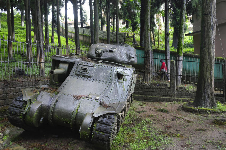 A woman walks past a Medium Tank M3 Grant that was abandoned when it went down this hill and crashed against a tree while climbing the Kohima Ridge to support British troops of the 2nd Division on May 6, 1944, in Kohima, India, Thursday, Aug. 13, 2020. In April 1944, 15,000 men from the 31st Division of Japan's Imperial Army commanded by General Sato arrived with the aim of taking over Kohima, a hill town that was also the headquarters of the British in the Naga Hills. The hill station, on the Indian border with Myanmar, was considered strategically important for Japanese advancement into India. The tank has been preserved in the exact position where it was abandoned. (AP Photo/Yirmiyan Arthur)