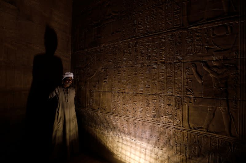 Abd El Naby, guard of Temple of Philae looks on beside Egyptian hieroglyphs carved for "Hapi" God of the Nile are seen on the wall in Aswan