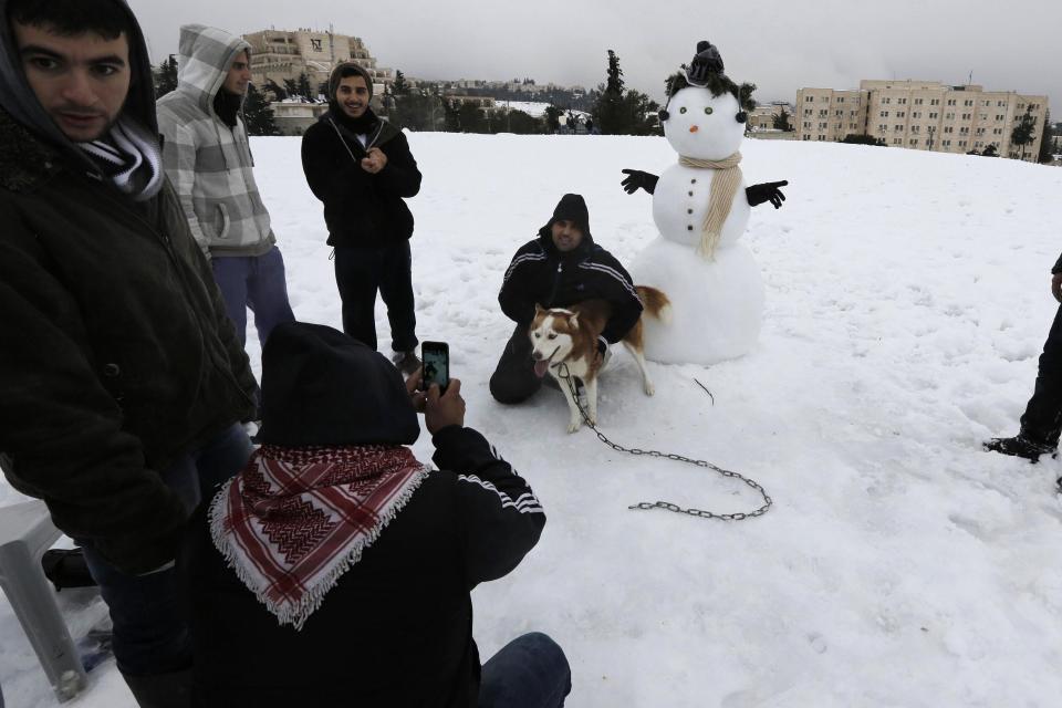 People take pictures of each other in the snow following a snowstorm at a park in Jerusalem December 14, 2013. Jerusalem's heaviest snow for 50 years forced Israeli authorities to lift a Jewish sabbath public transport ban on Saturday and allow trains out of the city where highways were shut to traffic. REUTERS/ Ammar Awad (JERUSALEM - Tags: ENVIRONMENT)