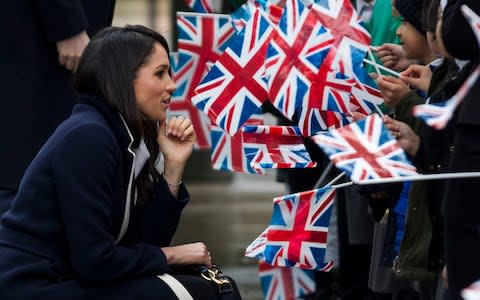Meghan Markle kneels as he chats to flag-waving children  - Credit: Heathcliff O'Malley for The Telegraph 