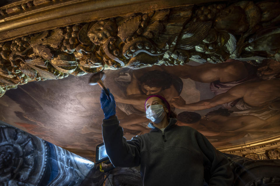 Restorer Romana Albini works, Wednesday, Dec. 6, 2022, in the Consiglio dei Dieci Hall inside Palazzo Ducale in Venice, northern Italy, on the gilded carved wooden ceiling surrounding Jacopo D'Andrea's 1863 copy of Paolo Veronese's oil on canvas 'Jupiter Hurling Thunderbolts at the Vices', confiscated by the art commissars of Napoleon Bonaparte and removed to Paris in 1797. (AP Photo/Domenico Stinellis)