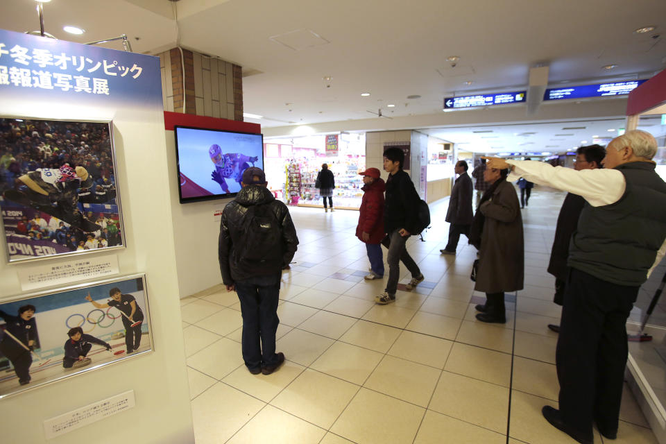 In this Wednesday, Feb. 19, 2014, photo, people watch a television showing a live broadcast of Japanese snowboarder Tomoka Takeuchi competing at the Sochi Winter Olympics in the women's snowboard parallel giant slalom final, in a concourse at Tokyo Station in Tokyo. The program is typical of the localized TV broadcasts in countries throughout the world during the Winter Olympics. The Japanese words at top left read: Sochi Winter Olympic Press Photo Exhibition. (AP Photo/Shizuo Kambayashi)