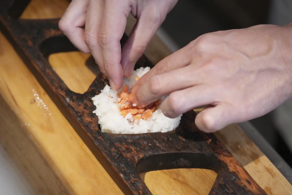 Yosuke Miura makes a rice ball with pieces of grilled salmon at Onigiri Asakusa Yadoroku, Tokyo's oldest onigiri restaurant, on June 3, 2024, in Tokyo. The word "onigiri" just became part of the Oxford English Dictionary this year. The humble sticky-rice ball, a mainstay of Japanese food, has entered the global lexicon. (AP Photo/Eugene Hoshiko)