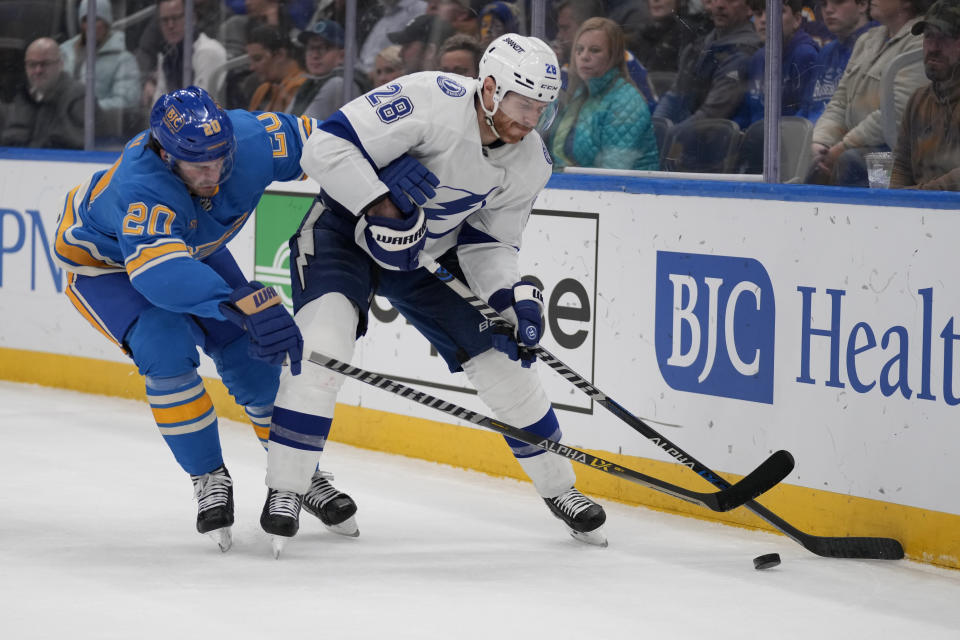 St. Louis Blues' Brandon Saad (20) and Tampa Bay Lightning's Ian Cole (28) chase after a loose puck along the boards during the second period of an NHL hockey game Saturday, Jan. 14, 2023, in St. Louis. (AP Photo/Jeff Roberson)