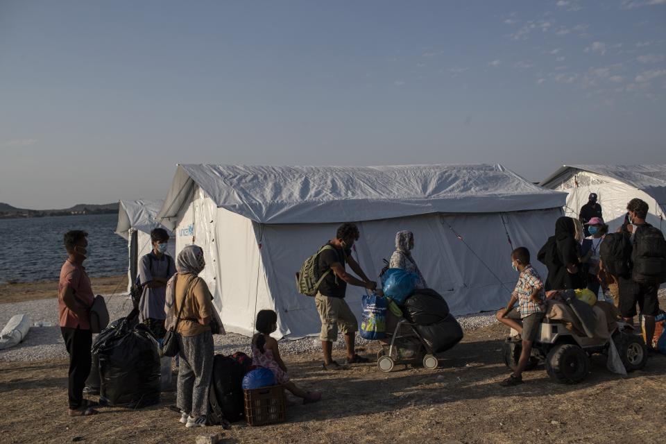 Migrants arrive at a temporary camp near Mytilene town, on the northeastern island of Lesbos, Greece, Saturday, Sept. 12, 2020. Greek authorities have been scrambling to find a way to house more than 12,000 people left in need of emergency shelter on the island after the fires deliberately set on Tuesday and Wednesday night gutted the Moria refugee camp. (AP Photo/Petros Giannakouris)