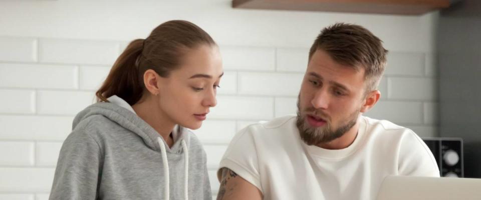 Focused young couple checking analyzing utilities bills sitting together at kitchen table, serious husband and wife reading bank loan documents