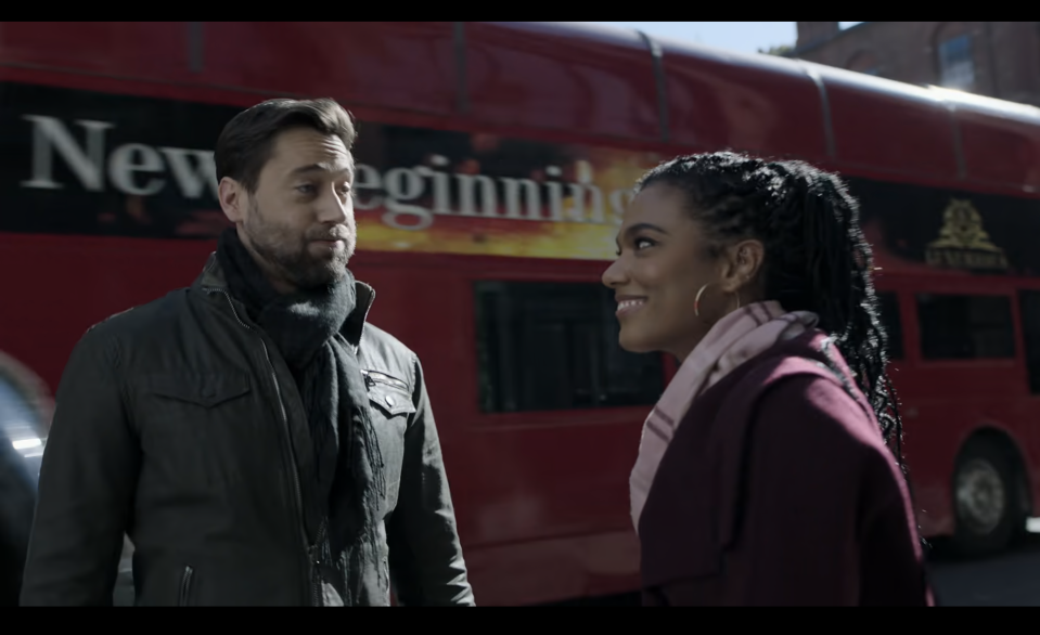 Ryan Eggold and Freema Agyeman standing face-to-face on a street with a double-decker bus in the background
