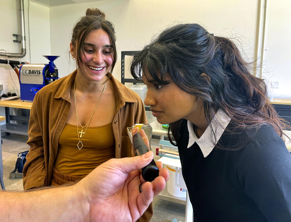 Timothy Styczynski, Head Roaster, UC Davis Coffee Center offers a smell of freshly ground coffee to Shrishti Chezhian, UC Davis Senior, right and graduating student Kiara DeGroen, at the Coffee Center at UC Davis in Davis, Calif. on Monday, June 17, 2024. The center which opened last month, is believed to be the first coffee-only research facility opened on any college campus in the U.S. (AP Photo/Haven Daley)