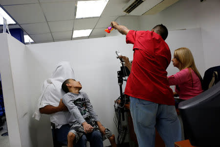 Miguel Anton (L covered) holds his son, Jose Gregorio Anton, 11, a neurological patient being treated with anticonvulsants, while workers takes a picture to him for his ID in La Guaira, Venezuela February 20, 2017. REUTERS/Carlos Garcia Rawlins