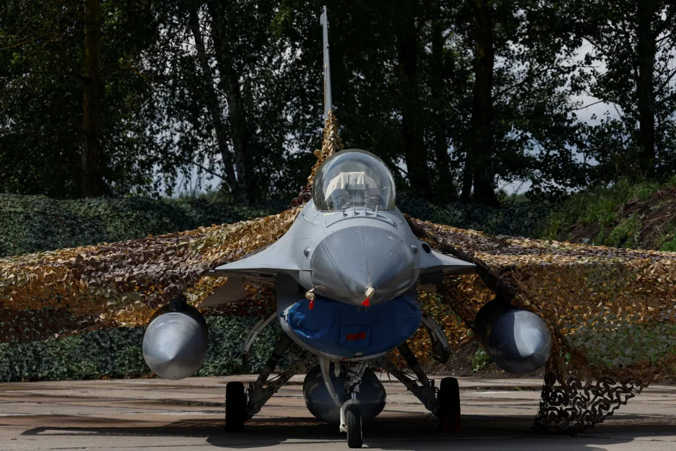 A fighter jet on the ground, its wings covered in camo netting.