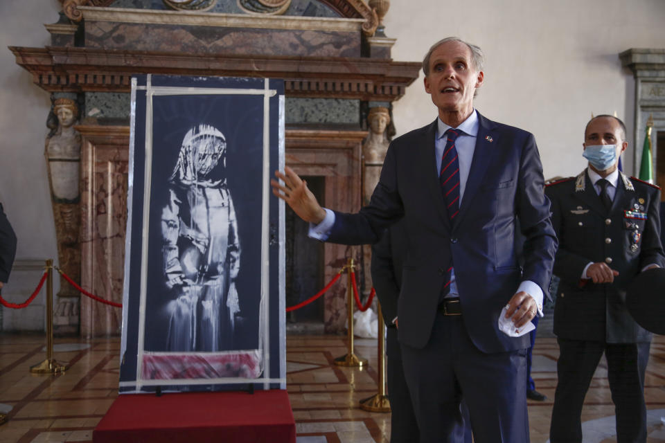 Franch Ambassador to Italy, Christian Masset, unveils a recovered stolen artwork by British artist Banksy, depicting a young female figure with a mournful expression, that was painted as a tribute to the victims of the 2015 terror attacks at the Bataclan music hall in Paris, during a ceremony at the French Embassy in Rome, Tuesday, July 14, 2020. (AP Photo/Domenico Stinellis)