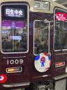 This 2024 image shows an ad on the front of a train, publicizing the upcoming World Expo 2025, in Osaka, Japan. The ad features the red-and-blue “Myaku-Myaku” mascot. (Katherine Roth via AP)