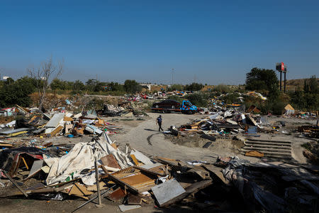 A police officer walks amidst debris as a truck tows an abandoned car at the Roma shanty town of El Gallinero, on the outskirts of Madrid, Spain, September 27, 2018. REUTERS/Susana Vera